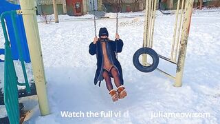 Naked tomboy in a fur coat swings on a swing in winter