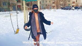 Naked tomboy in a fur coat swings on a swing in winter